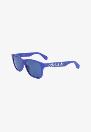 Occhiali da sole Adidas blu con lenti scure e logo Adidas bianco sulle aste, su sfondo bianco.