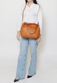 Handtas van gehard leer in een afgeronde vorm, met een korte bovenhandgreep en een verstelbare schouderriem; gladde textuur en gestikte details.