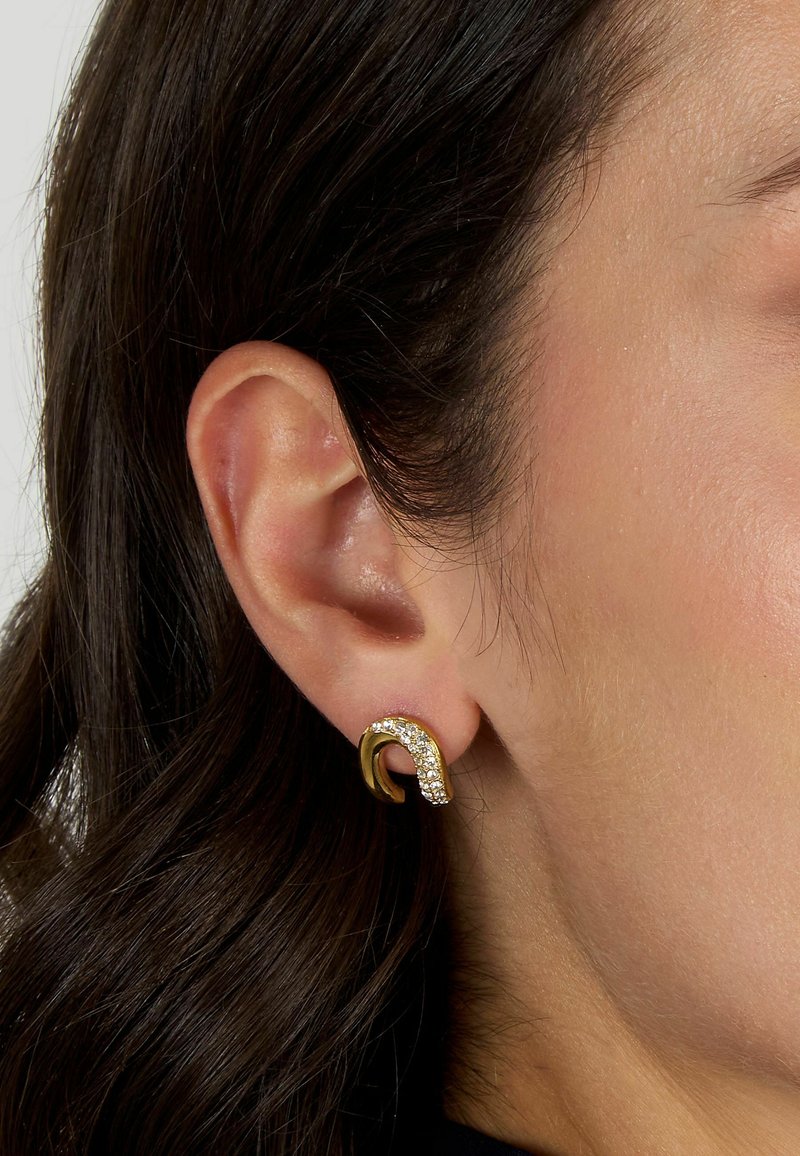 Orecchini color oro con un design curvo, impreziositi da cristalli trasparenti, che presentano una superficie texturizzata e una finitura lucida.