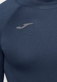 Tengerészkék, hosszú ujjú sportfelső rugalmas anyagból. Slim fit szabású, a mellkason egy kis, világosszürke logó található. Sima tapintású.