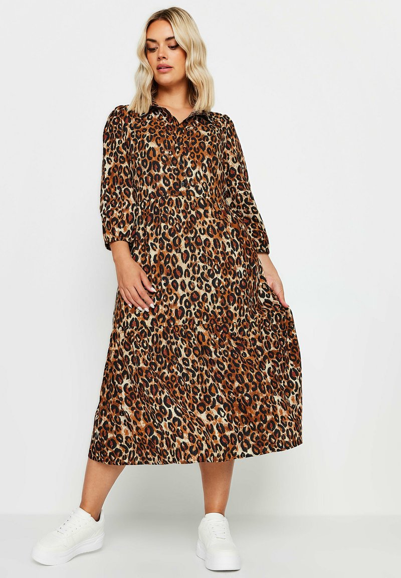 Keski-pituinen leopardi-kuosisukki, jossa on kaulus, 3/4-hihat ja laskostettu hame, yhdistettynä valkoisiin lenkkareihin. Kangas on sileä.