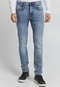 Ljust blå denimjeans med slim fit, med fem fickor, kontrasterande sömmar och blekta områden för en sliten look. Burit med svarta sneakers.