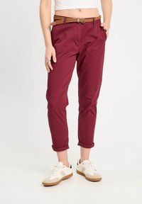 Bordeaux bomuldsbukser med opsmøg, parret med et vævet brunt bælte. Hvide sneakers med beige accenter og en sort hældetalje.