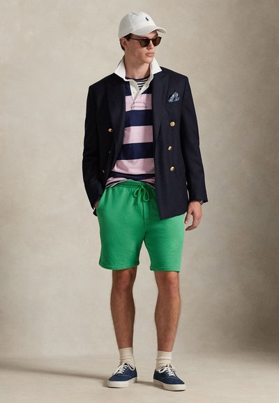 Μπλε μπλέιζερ με χρυσά κουμπιά πάνω από ροζ και μπλε ριγέ πόλο, πράσινες βερμούδες, άσπρο καπέλο και γυαλιά ηλίου. Μπλε αθλητικά παπούτσια και λευκές κάλτσες ολοκληρώνουν την εμφάνιση.