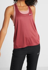 Bordowy sportowy tank top wykonany z lekkiego materiału z dekoltem w kształcie litery U. Na piersi znajduje się małe, srebrne logo Nike oraz oddychające siateczkowe akcenty.