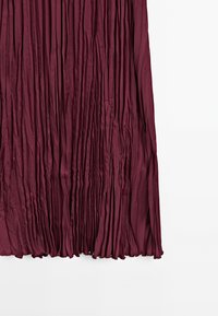 Jupe plissée bordeaux avec une surface lisse et texturée, mettant en valeur des plis verticaux et un ourlet légèrement effiloché.