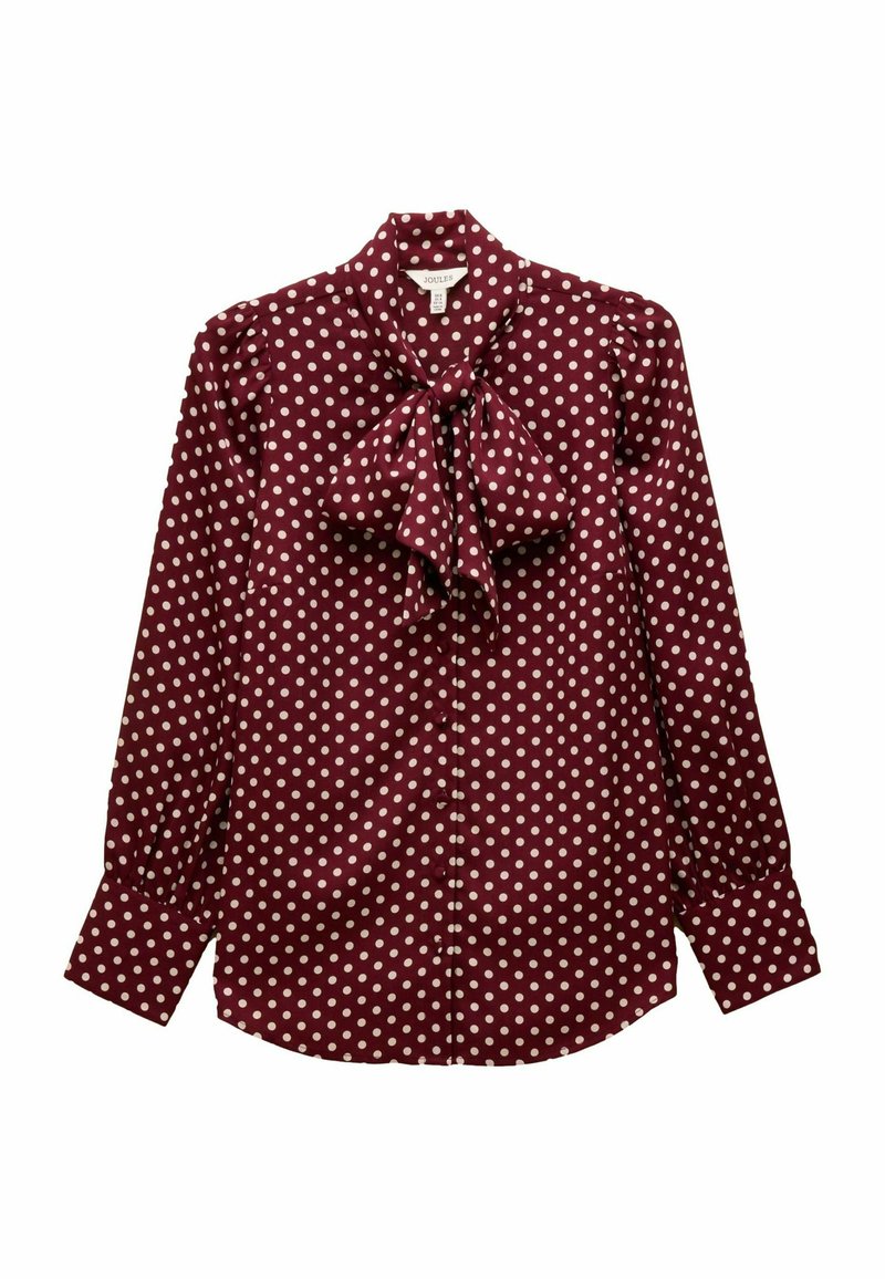 Burgundy blouse with white polka dots. Features a tied bow at the neck, buttoned front, and gathered sleeves for a structured shape.