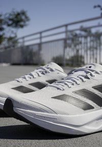White athletic shoes with black accents, mesh upper, textured surface, and thick sole. Features three black stripes on each side.