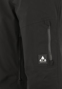 Schwarze wasserdichte Jacke mit einer zippten Tasche, glatter Textur und einem Etikett mit einem Berglogo auf der linken Seite.