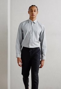 Striped button-up shirt in blue and white cotton fabric, paired with dark navy pants. The outfit features a classic collar and long sleeves.