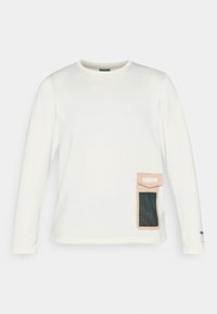 Camisa blanca de manga larga con un patrón de rayas texturizadas. Presenta un bolsillo beige con una inserción de malla en el lado izquierdo.