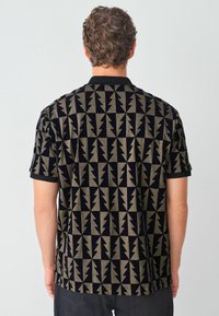 Cămașă cu mânecă scurtă, care prezintă un model geometric îndrăzneț în negru și auriu, cu un material texturat, guler plat și manșete ale mânecilor în contrast.