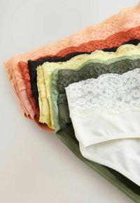 Stos złożonej damskiej bielizny z koronkowym wykończeniem w kolorach białym, zielonym, żółtym, czarnym, rdzawej czerwieni i brzoskwiniowym na jasnej powierzchni.