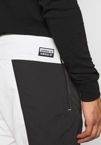 Svartvita sportiga joggers har en elastisk midja, sidopaneldesign och en broderad Adidas-logotyp på bakfickan.