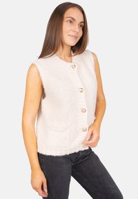 Helles rosa, flauschige Weste mit rundem Halsausschnitt, fünf Knopfverschluss, zwei Fronttaschen und einer strukturierten Oberfläche, kombiniert mit dunklen Jeans.