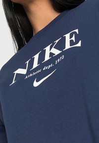 Mörkblå bomulls långärmad skjorta med vit "NIKE" text och logotyp. Enkel crew neck design med detalj av "Athletic dept. 1972."