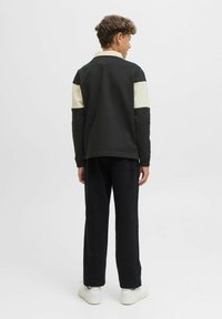 Fekete és krém színű blokkolt sweaterviselő, gallérral, fekete nadrággal és fehér sportcipővel párosítva, hátulról mutatva.