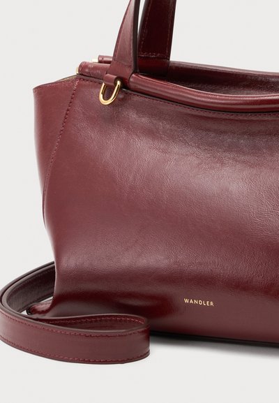 Sac à main en cuir bordeaux avec poignées supérieures, bandoulière amovible, anneau en métal doré et logo "Wandler" en bas à droite sur le devant.