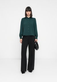 Grønn skjorte med krage og puffermer, kombinert med svarte vide bukser. Aksesorrert med en liten svart veske.