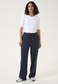Navy blauwe joggers gemaakt van zachte stof, met een trekkoord in de taille, brede benen en zijnaad. Gepaard met een aansluitend wit topje.