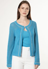 Hellblaues Strickcardigan mit offenem Muster, rundem Halsausschnitt und Schlüsselaugen-Detail. Verfügt über einen kontrastierenden Saum und eine weiche Textur.