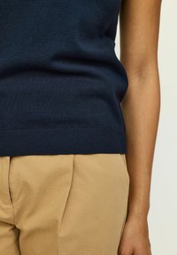 Pull bleu marine avec un ourlet côtelé et une texture lisse, associé à un pantalon beige clair avec des plis et des poches latérales.