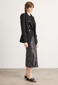 Svart dobbeltrad blazer med gullknapper, paret med en knelang leopardskrik av satin og svarte sandaler med blokk-hæl og åpne tær.