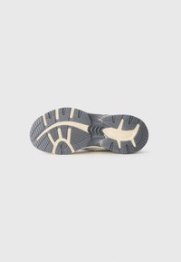 Semelle de chaussure en caoutchouc texturé gris avec des accents crème. Présente de profonds sillons et un design incurvé pour une traction et un soutien.