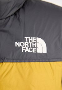 Puffer jacket featuring a color-block design with a dark gray upper and mustard yellow lower sections; embroidered white logo on chest.