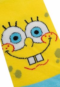 Calzini di cotone gialli con un design cartoon dettagliato del volto di un personaggio, con occhi blu, linee nere e piccoli punti verdi.