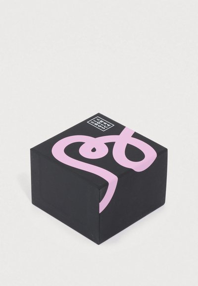 Fekete négyzet alakú csomagolás lekerekített sarkokkal, központi eleme egy feltűnő rózsaszín csavargás, a felső sarokban pedig egy kis fekete négyzet logó található.