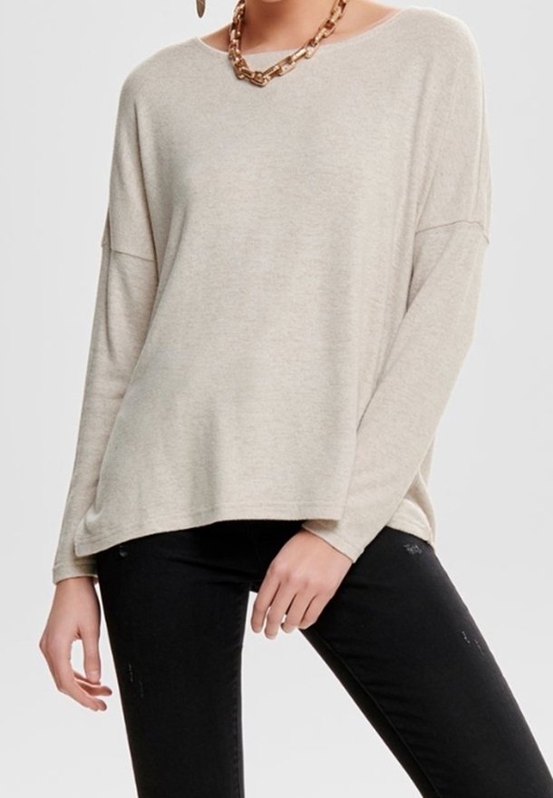 Pull en tricot beige à coupe décontractée, avec des manches longues et un col large. Porté avec un jean foncé et un collier chaîne épais.