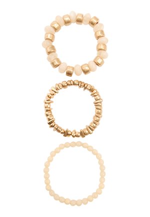 Trzy rozciągliwe bransoletki z koralików w odcieniach bieli i złota ułożone pionowo na białym tle.
