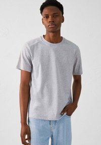 Camiseta gris de manga corta hecha de tejido suave, con un cuello redondo y una forma ajustada. Textura suave con un detalle de marca sutil.