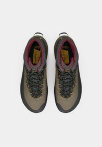 Brūni un pelēki kāpšanas apavi ar teksturētu augšdaļu, dzelteniem akcentiem, gumijas purngalu un mīkstu apkaklīti. Šņores centrā nodrošina drošu piegulšanu.