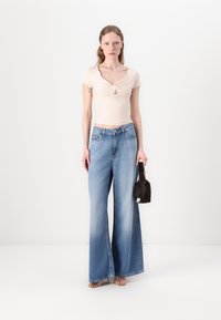 Top de punto beige con detalle retorcido, combinado con unos vaqueros de pierna ancha en azul claro y un pequeño bolso negro. Tejidos suaves, ajuste relajado, estilo casual.