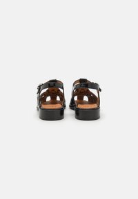 Svarta lackskinnsandaler med öppen design, ankelrem, spänningsdetalj och låg klack. Insidan har en beige lädersula.