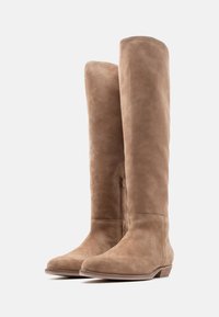 Ζευγάρι ψηλές μπεζ μπότες από σουέτ με χαμηλά στρωμένα τακούνια και πλαϊνό φερμουάρ σε λευκό φόντο.