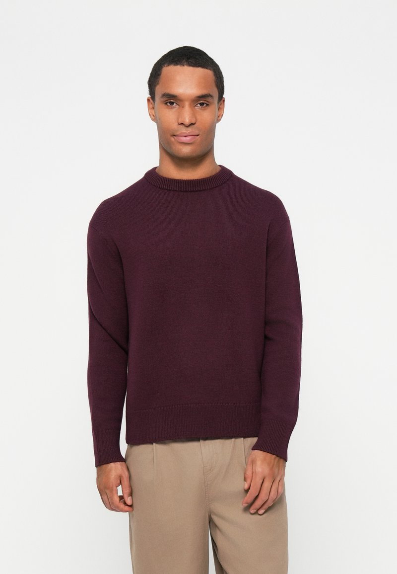 Μαρούλι πλεκτό πουλόβερ με στρογγυλή λαιμόκοψη και μακριά μανίκια, διαθέτοντας ribbed μπούστο και μανσέτες, σε συνδυασμό με μπεζ παντελόνι.