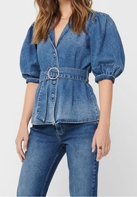 Light blue denim top with puffed sleeves, v-neck, and belted waist featuring a rhinestone buckle. Paired with matching jeans.
