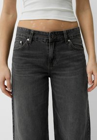 Visoko pasovi, široke nogavice iz jeansa v temno sivi barvi. Imajo pet žepov, kovinsko gumb in kontrastne šive. Gladka tekstura z sproščenim krojem.