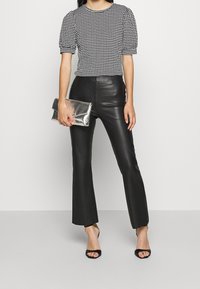Černo-bílý top s houndstooth vzorem a krátkým rukávem, kombinovaný s přiléhavými černými kalhotami z umělé kůže, které se rozšiřují dolů. Modelka drží metalickou stříbrnou kabelku.