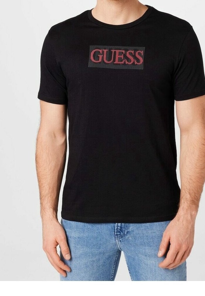 T-shirt en coton noir avec un logo "GUESS" rouge au centre. Manches courtes et col rond. Coupe décontractée avec une texture lisse.