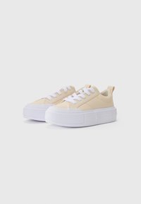 Beige vászon sportcipők vastag fehér gumitalppal, fehér fűzőkkel és hátsó húzófüllel a könnyű felvétel érdekében. Minimalista dizájn.