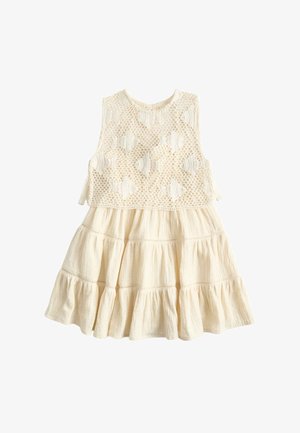 Vestido sin mangas crema con falda de volantes texturizados y cuerpo de encaje de crochet con patrones de conchas, cierres de lazo en los costados.