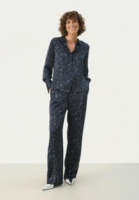 Navy blå leopardprint pyjamassat i blødt stof; har en knap-up langærmet skjorte og løstsiddende bukser. Pyntet med lommer.