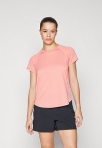 Kortermet treningsgenser i lys rosa, med teksturert stoff og rund halsutringning. Kombinert med svarte trening shorts for kontrast.
