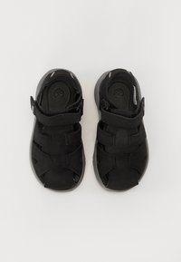 Sandalias negras de cuero con suela de goma, que cuentan con correas ajustables y diseños troquelados para la ventilación.