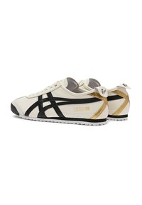 Sneakers with a cream leather upper, black stripes, and gold accents. Features a rounded toe and textured sole for grip. Model: Mexico 66.