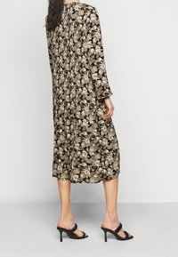 Svart blommig klänning med långa ärmar, prydd med ett mönster av guld- och gräddfärgade blommor. Tyget är lätt och designen är knälång.